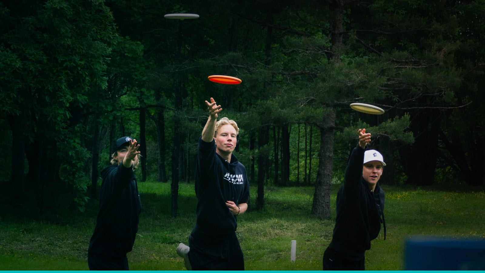 Kolme frisbeegolfpelaajaa puttaavat kiekkoa kohti koria.