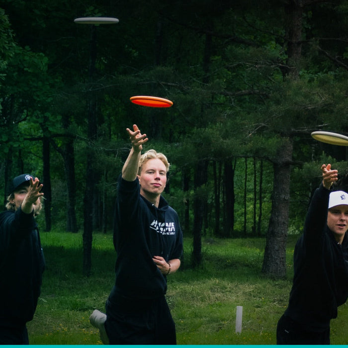 Kolme frisbeegolfpelaajaa puttaavat kiekkoa kohti koria.